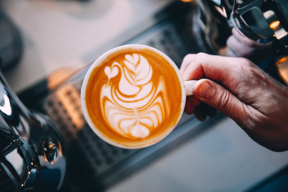 A barista's hands finishing a latte at the espresso machine