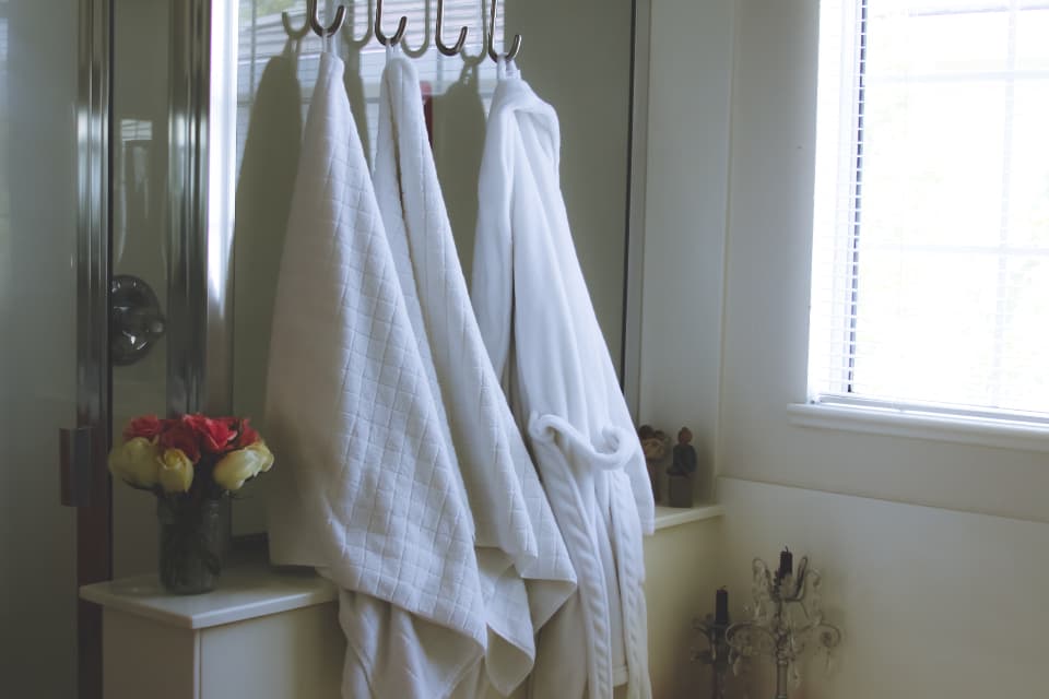 White bathrobes hanging on hooks beside a bright window