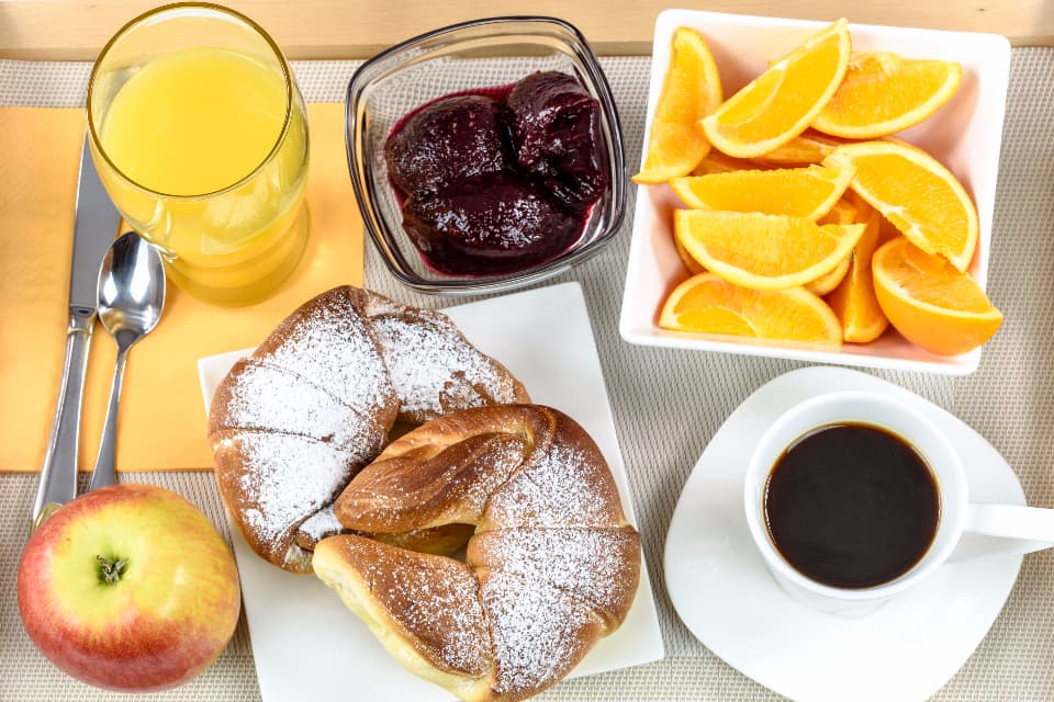 A breakfast table seen from above: coffee, pastries, orange juice and sliced fruit