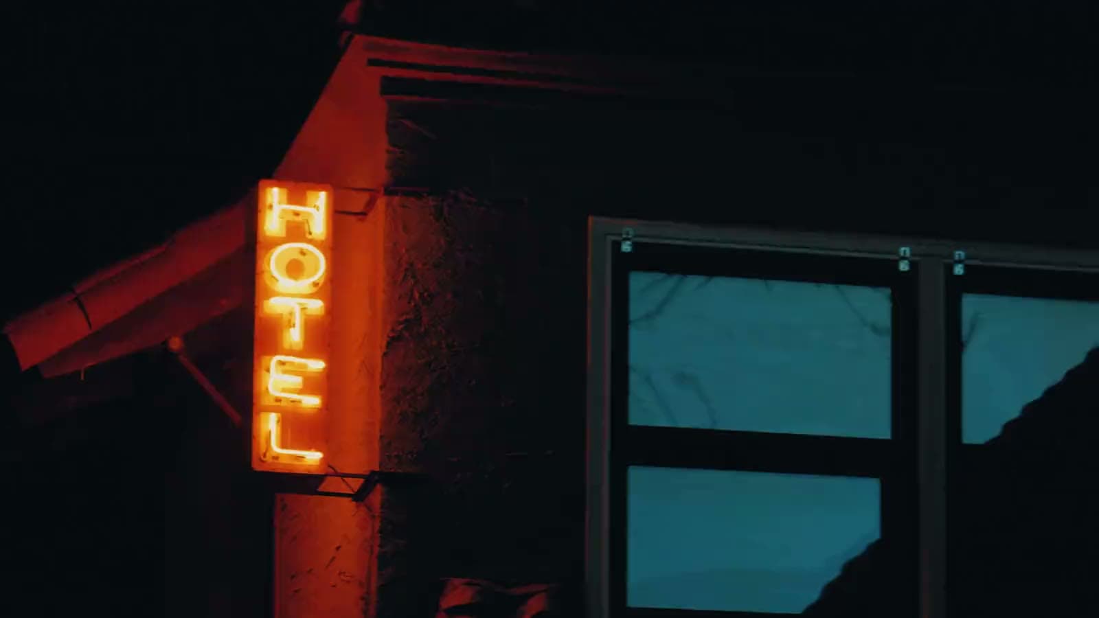 The hotel's neon sign on a dark corner, two lit windows beside it