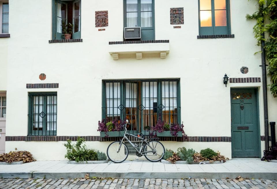 A bicycle leaning against a white townhouse with flower boxes