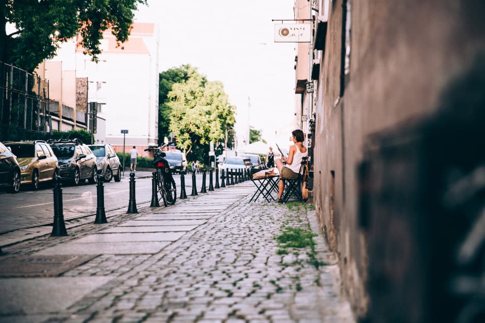 A cobbled side street with a cafe table and a tree in the morning light