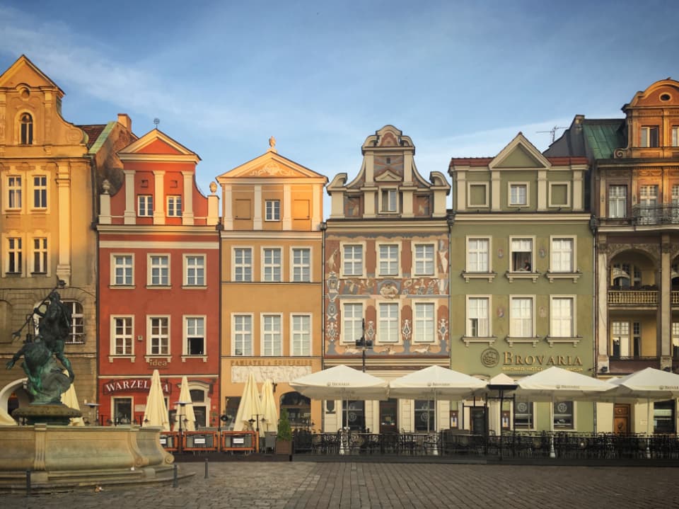 Narrow painted townhouses around a square with cafe umbrellas