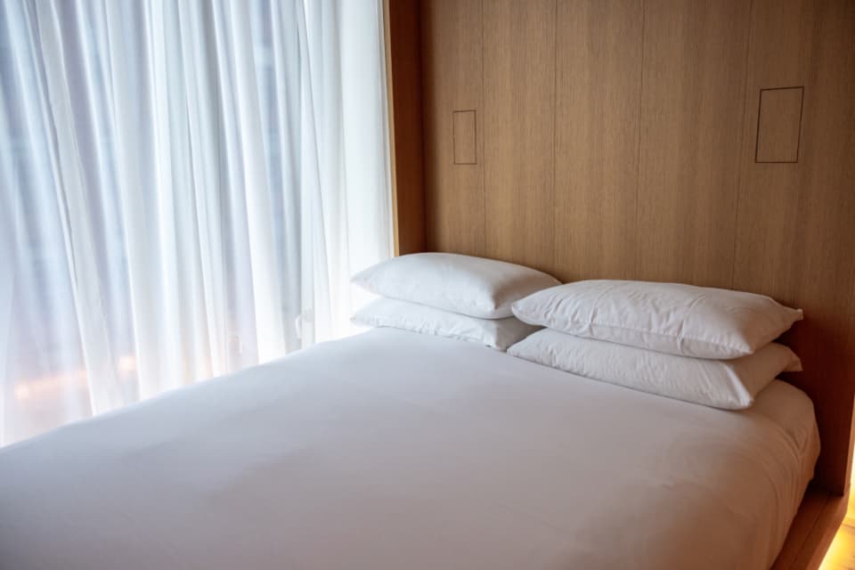 A white-linen double bed under a tall window with sheer curtains