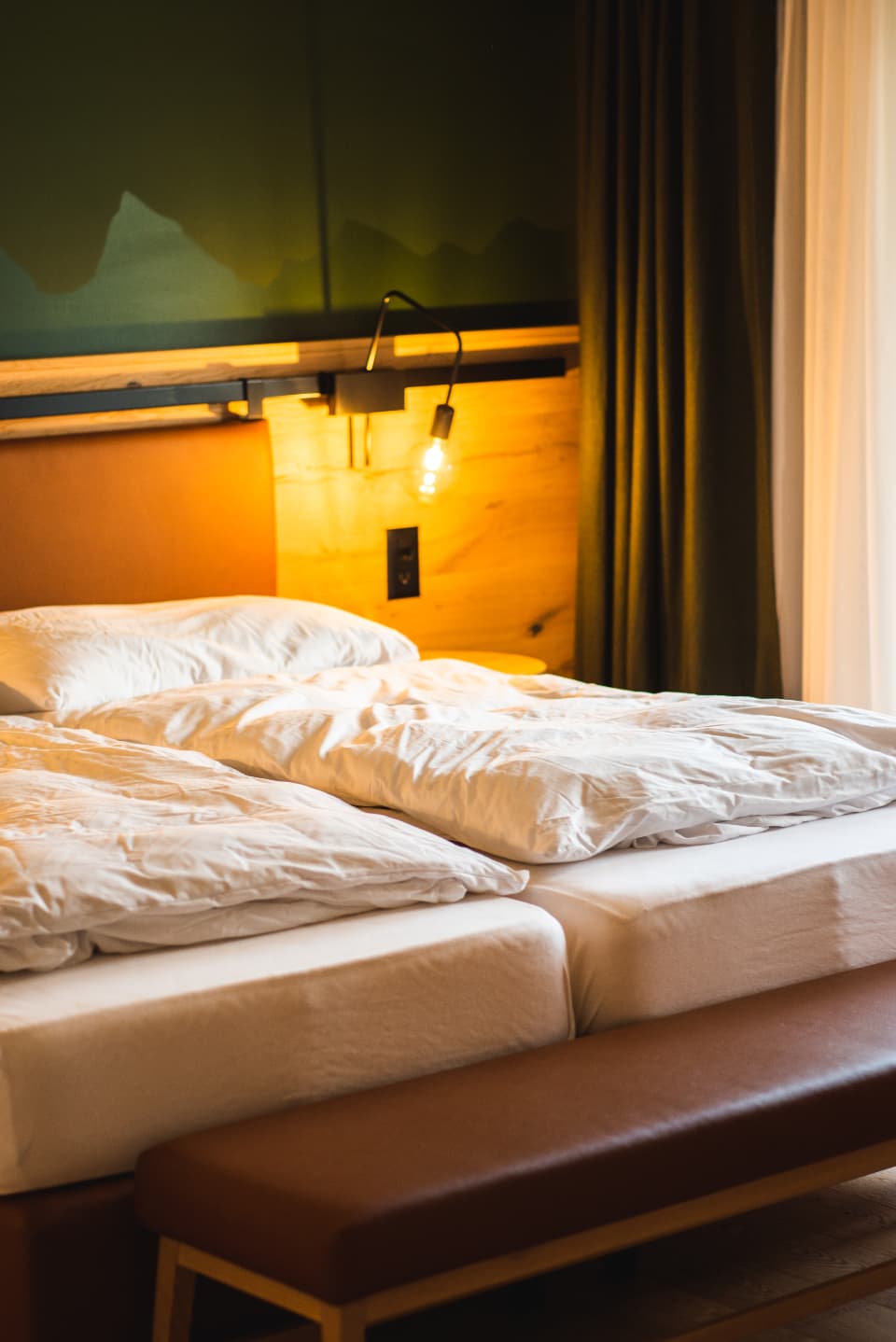 Two single beds with pink cushions and a lit bedside lamp between them